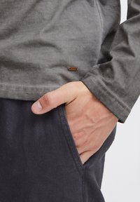 Graues Langarmshirt mit einem Stoffetikett. Das Shirt hat einen lässigen Schnitt, eine glatte Textur und wird mit dunklen Hosen kombiniert.