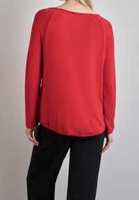 Czerwona bluza z długim rękawem wykonana z fakturowanego materiału, z zaokrąglonym dołem i luźnym fasonem, zestawiona z czarnymi spodniami. Swobodny i wygodny design.