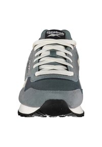 Zapatillas Reebok con una parte superior de textil gris, cordones blancos, una lengüeta acolchada y una suela de goma negra con un patrón texturizado.