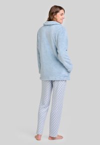 Chaqueta de piel sintética azul claro con cuello, combinada con pantalones de pijama de estampado en gris y blanco, que presentan un delicado motivo.