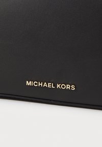 Borsa in pelle nera con branding dorato "MICHAEL KORS", caratterizzata da una texture liscia e un design minimalista.