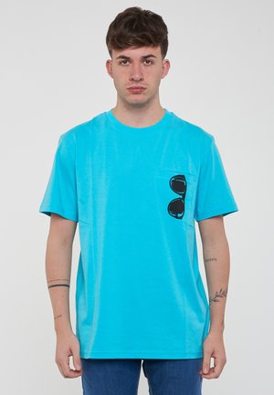 T-shirt in cotone turchese con maniche corte, caratterizzato da una tasca sul petto con una grafica di occhiali da sole neri. Vestibilità rilassata, texture liscia.