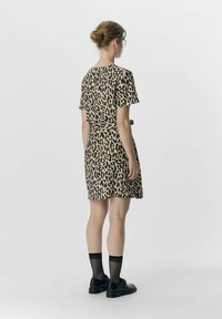 Robe à imprimé léopard avec des manches courtes, taille cintrée et ourlet au genou, en tissu doux, associée à des chaussures noires et des chaussettes.