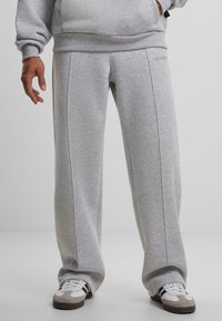 Graue Sweatpants aus weichem Stoff, mit lockerer Passform, Seitennähten und einem dezenten Logo in der Nähe des Bundes. Kombiniert mit weißen Sneakern.