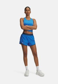 Un débardeur de sport bleu associé à un short en maille bleu avec une ceinture contrastante, et des baskets blanches avec des semelles texturées.