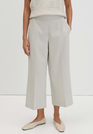 Frau trägt hellgraue, weit geschnittene, gekürzte Hose mit seitlichen Taschen, kombiniert mit beigen, gerafften Ballerinas und einem ärmellosen Stricktop.