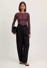 Langsleeve bordeauxrood top met stiksel details, gecombineerd met hoge zwarte broek, een zwarte riem en een zwarte clutch tas. Zwarte sandalen met hak.
