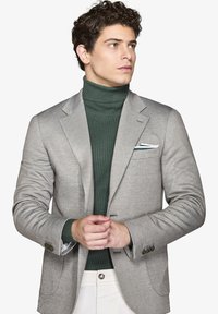 Grå herringbone blazer med grøn ribbet turtleneck. Blazeren har to knapper og en hvid pocket square. Glat, skræddersyet pasform.