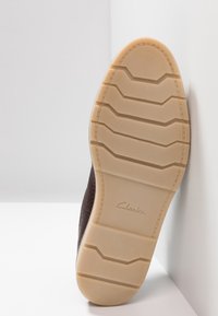 Semelle de chaussure marron texturée avec une finition à motif semblable à du caoutchouc ; présente des crêtes rembourrées et un logo "Clarks" embossé près du talon.
