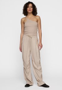 Beige geribbelde tanktop met één schouderband, gecombineerd met losvallende, lichtbeige broek met een koord in de taille en zijzakken.