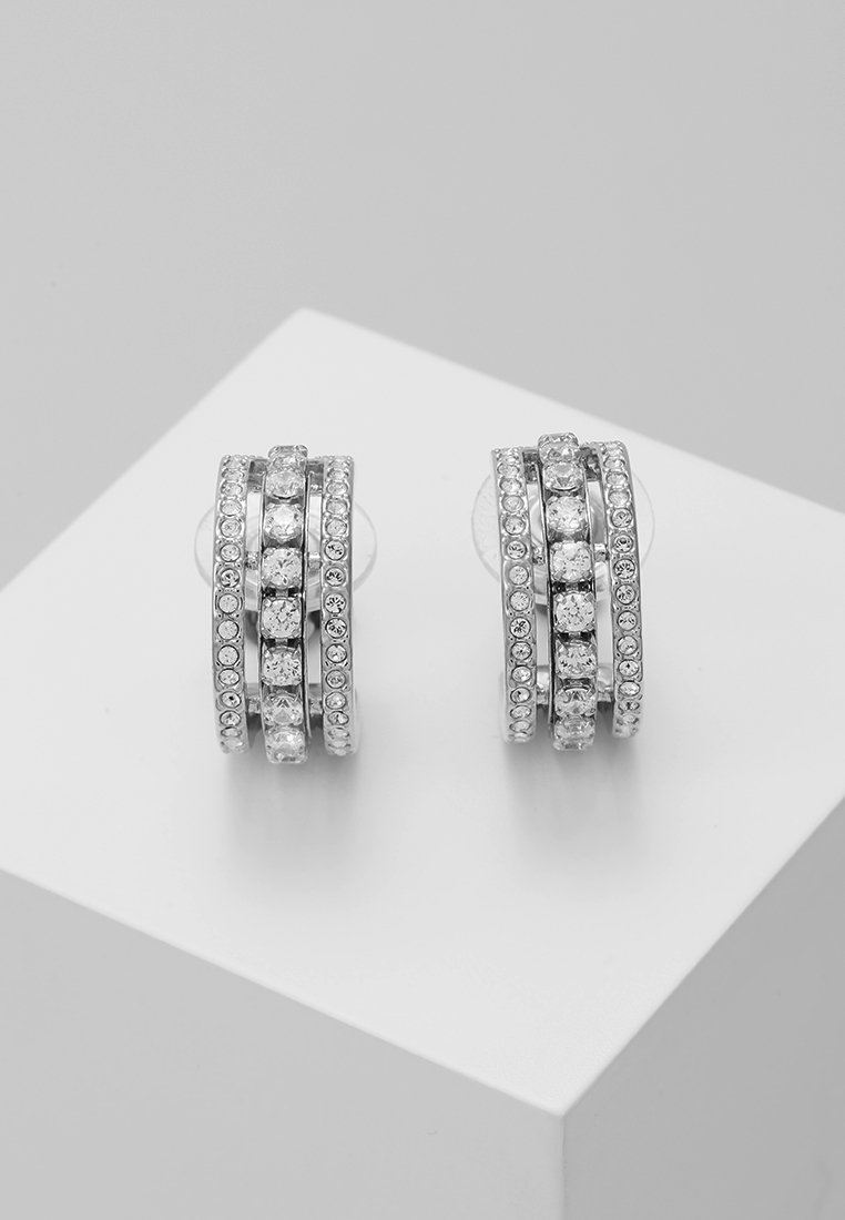 Boucles d'oreilles créoles en argent avec trois rangées de cristaux ronds transparents sur un présentoir blanc.