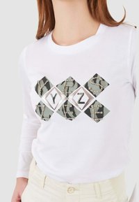 Maglietta bianca a maniche lunghe con un design geometrico decorato da motivi camouflage e lettere in perline "Y", "Z" e "E" sul davanti.