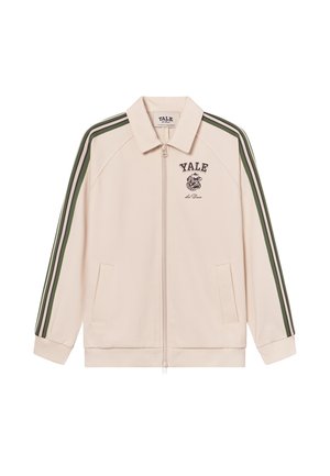 Veste zippée beige clair avec des rayures vertes et blanches sur les épaules. Elle arbore un logo de Yale sur la poitrine et deux poches latérales.