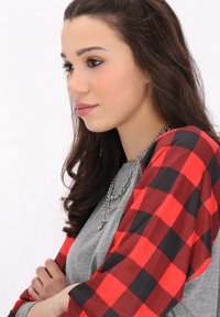 Långärmad topp med röd och svart rutmönstrad ärmar, grå kropp och ett silverhalsband. Texturerad tyg och avslappnad passform.