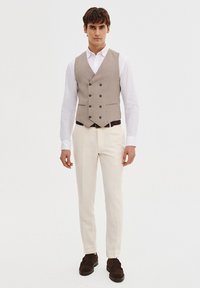 Beżowy, podwójnie zapięty kamizelka na białej koszuli, zestawiona z kremowymi spodniami. Brązowe skórzane buty dopełniają strój. Prosty, dopasowany krój.