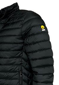 Chaqueta acolchada negra con costuras horizontales, cuello alto y bolsillo con cremallera lateral. Presenta un parche de logo amarillo en la manga.
