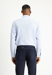 Jasnoniebieska koszula w paski z długimi rękawami i mankietami na guziki, w zestawieniu z ciemnogranatowymi spodniami z elastycznym pasem i tylnymi kieszeniami.