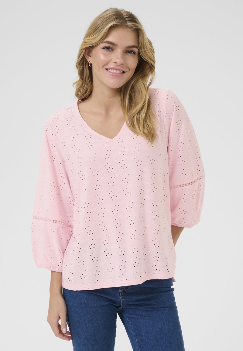 Blusa di cotone rosa con scollo a V, maniche a puff di tre quarti e motivi a occhio ricamati su tutta la superficie. Texture morbida e vestibilità rilassata.