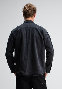 Zwarte denim overhemd met lange mouwen en een knoopsluiting bij de manchetten, voorzien van een klassieke kraag en een gestructureerde afwerking van de stof.