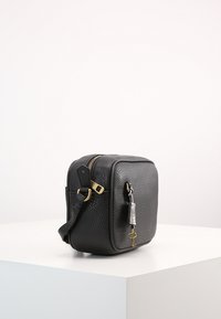Black leather crossbody bag with textured finish, gold-tone hardware, and a decorative silver keychain. Square shape with adjustable strap.