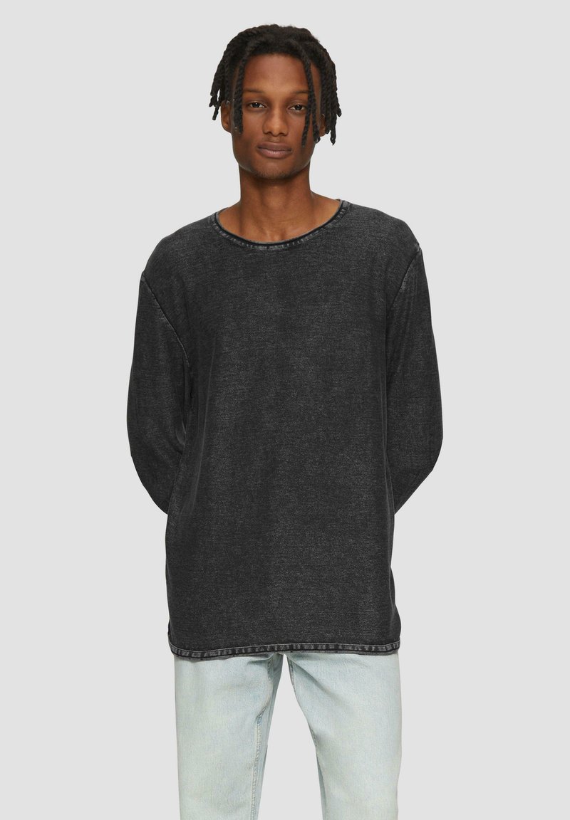 Zwarte longsleeve shirt met een ronde hals en een losse pasvorm. Zachte stof met zichtbare stiksels rond de kraag en de zoom.