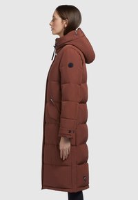 Lang, gewatteerde donkeroranje jas met een capuchon, voorzien van een rits aan de voorkant, zijzakken en een logo patch op de linker mouw. Glad van textuur.