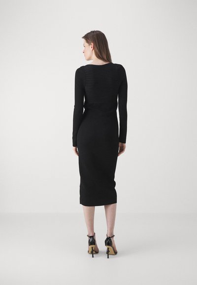 Μαύρο φόρεμα με μακριά μανίκια και υφασμάτινη πίσω πάνελ, εφαρμοστή σιλουέτα, μήκος μέχρι το γόνατο, συνδυασμένο με γυαλιστερές μαύρες στιλέτο γόβες.