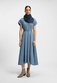 Blue pleated dress with short sleeves and a V-neck, cinched at the waist, paired with a dark scarf and beige ankle boots.