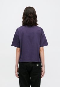 Fioletowa krótka koszulka z krótkimi rękawami, wykonana z bawełny, z okrągłym dekoltem i małą metką z logo marki na plecach.
