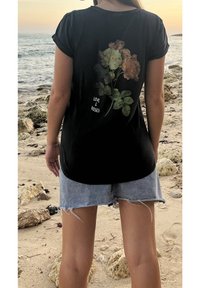Černé tričko s krátkým rukávem s květinovým vzorem růží v béžové a krémové barvě, označené nápisem "LÁSKA A RŮŽE", spárované se světlými džínovými šortkami.