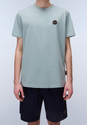 Hellgrünes Baumwoll-T-Shirt mit Rundhalsausschnitt und kurzen Ärmeln. Verfügt über ein rundes Patch auf der linken Brust und ein seitliches Etikett.