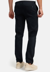 Dunkelblaue Baumwollhosen mit geradem Schnitt. Verfügt über Gesäßtaschen und schlichte Nähte. Kombiniert mit hellbeigen Sneakers.