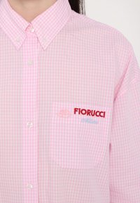 Ροζ πουκάμισο με καρό φινίρισμα και κλειστό γιακά· διαθέτει τσέπη με κόκκινη κεντημένη ένδειξη "Fiorucci Milano" και λευκά κουμπιά.