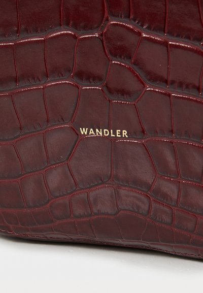 Μπορντό δερμά�τινη τσάντα χειρός με γυαλιστερή, ανάγλυφη υφή κροκοδείλου. Διαθέτει χρυσό κείμενο που γράφει "WANDLER" κοντά στο κάτω μέρος.
