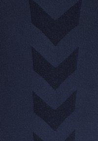 Donkerblauwe gebreide stof met verhoogde chevronpatronen. De textuurdetails voegen diepte toe aan het gladde oppervlak van het materiaal.