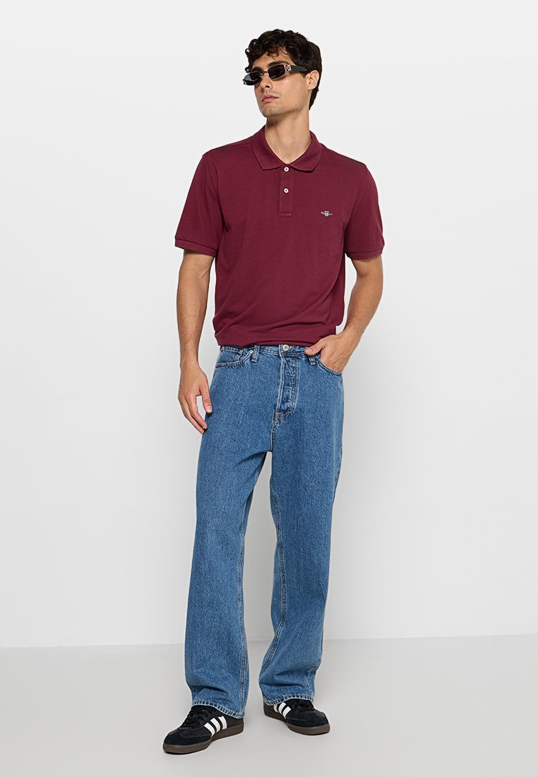 Polo bordeaux avec col et trois boutons, associé à un jean droit bleu clair et des baskets noires avec des rayures blanches.