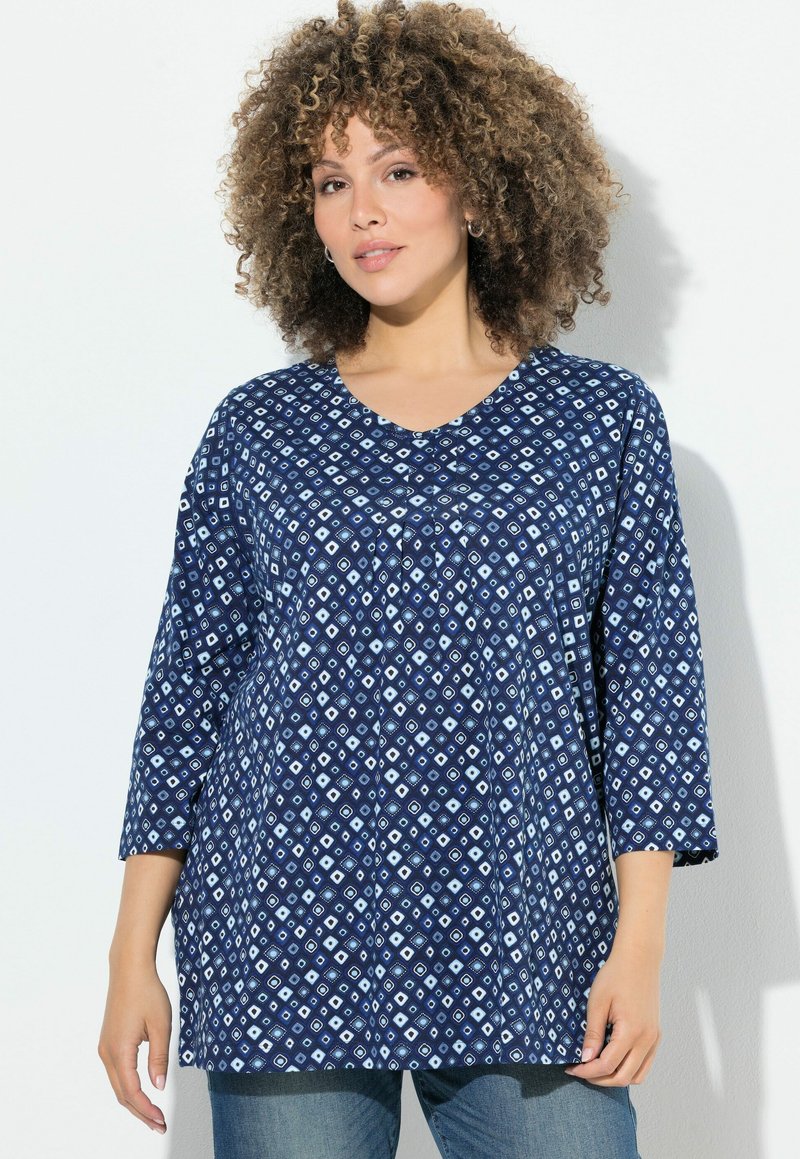 Tunic blu navy con motivo a diamante in azzurro chiaro. Presenta un scollo a V, maniche a tre quarti e una vestibilità comoda. Texture del tessuto morbida.
