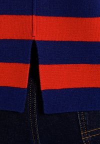 Sweter w paski z dzianiny, z naprzemiennymi czerwonymi i granatowymi poziomymi paskami oraz rozcięciem po boku u dołu. Miękka faktura, casualowy fason.