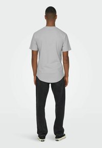 Gray short-sleeve t-shirt with a curved hem, paired with black straight-leg jeans and black sneakers, viewed from the back.