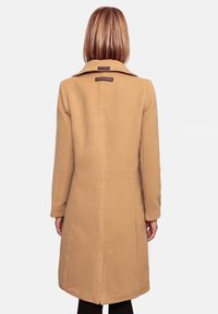 Beige, middellange jas gemaakt van zachte stof. Heeft een kraag met punten, twee achterlabels en een rechte snit met zijzakken.