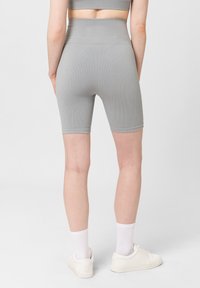 Pantalones cortos de ciclismo grises de canalé con una cintura alta, que presentan una textura suave y un ajuste ceñido, combinados con zapatillas blancas y calcetines.
