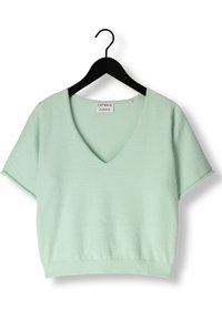 Light green, short-sleeve pullover top with a V-neck, made from soft textured fabric. Features a ribbed hem and side slits. Brand tag visible.