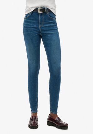 Schmale blaue Denim-Jeans mit hoher Taille, leichtem Verblassen und Fünf-Taschen-Design. Kombiniert mit einem schwarzen Gürtel und braunen Loafers.