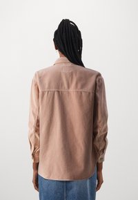 Rust-colored corduroy shirt with a collar, long sleeves, and buttoned cuffs. Features vertical ribbing and a straight back design.