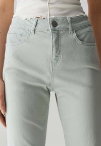 Jeans in denim verde chiaro con vita alta, dotati di tasche frontali, chiusura con bottone e una trama sottile.