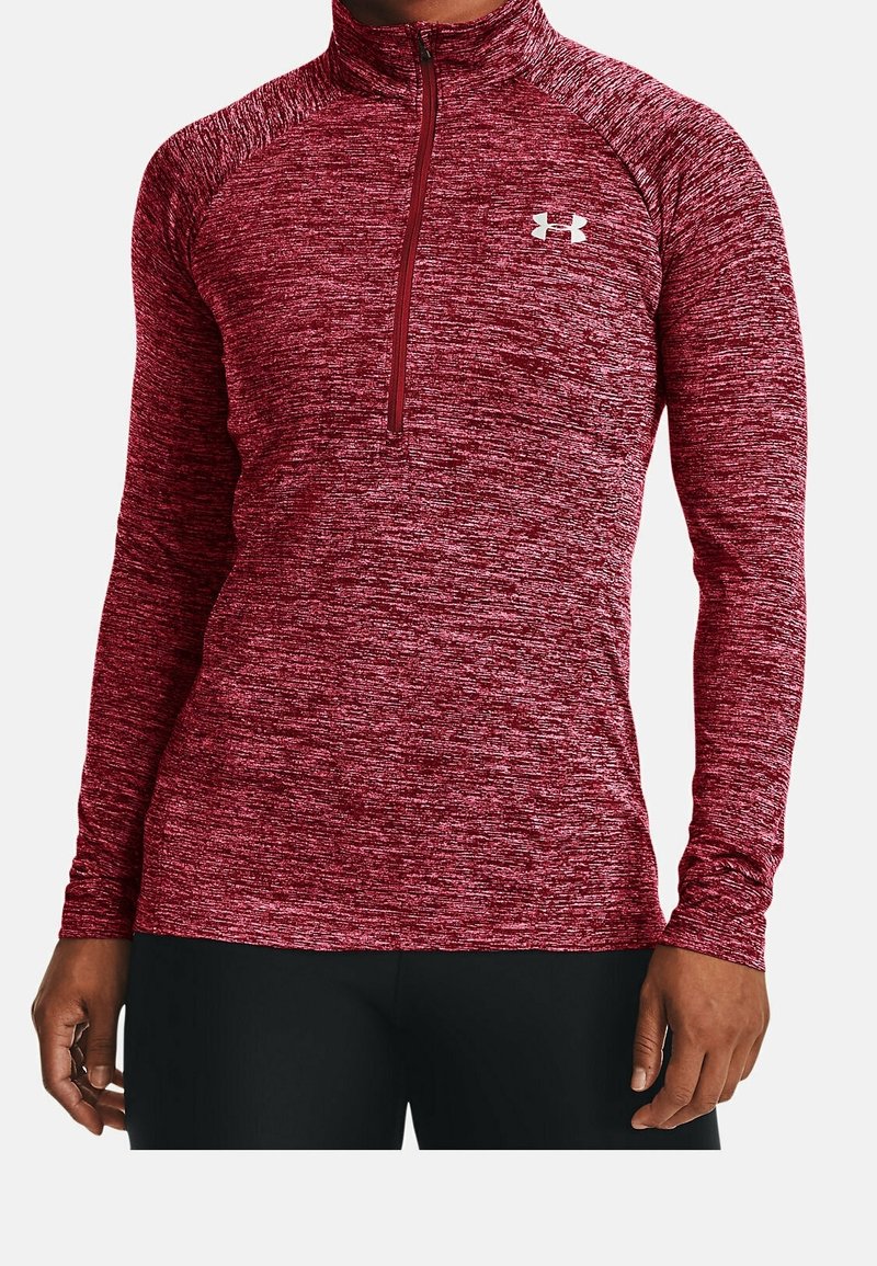 Uomo che indossa una maglietta a maniche lunghe color bordeaux melangiato con zip trimestrale aderente e logo bianco di Under Armour sul petto, abbinata a pantaloni neri.