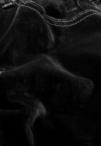 Zwarte fluwelen stof met een fijne textuur en subtiele glans, met zachte plooien en stikdetails, die de luxueuze uitstraling benadrukken.