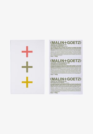 Weißer Kasten mit einem Design aus roten, grünen und gelben Pluszeichen; drei weiße Seifenstücke mit grünen Textetiketten, die mit Hydration und Exfoliation versehen sind.