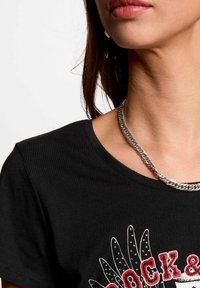 T-shirt in cotone nero con scollo rotondo, caratterizzato da una grafica con accenti rossi e argentati, abbinato a una collana in argento.