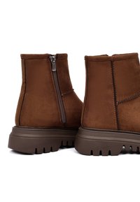 Bruine suede enkellaarsjes met een zijrits, stevige bruine rubberen zool en versterkte stiksels langs de naden.